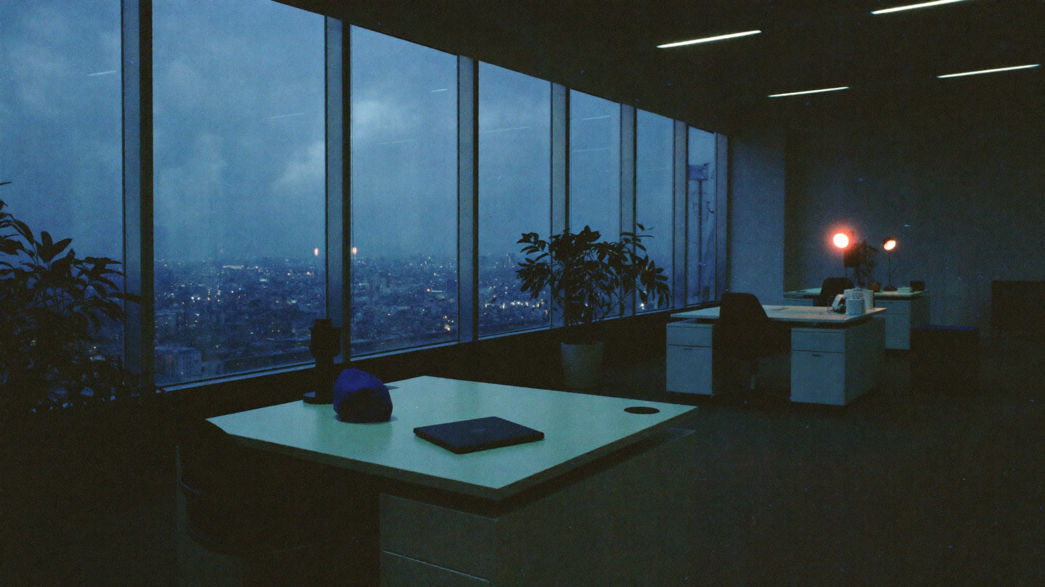 O escritório vazio no fim da tarde, com o notebook fechado sobre a mesa e as luzes da cidade na janela