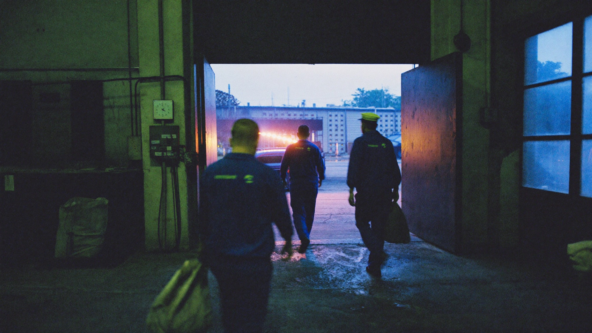 Madrugada na entrada de uma metalúrgica: o turno chega, e o relógio de ponto fica na parede ao lado da porta